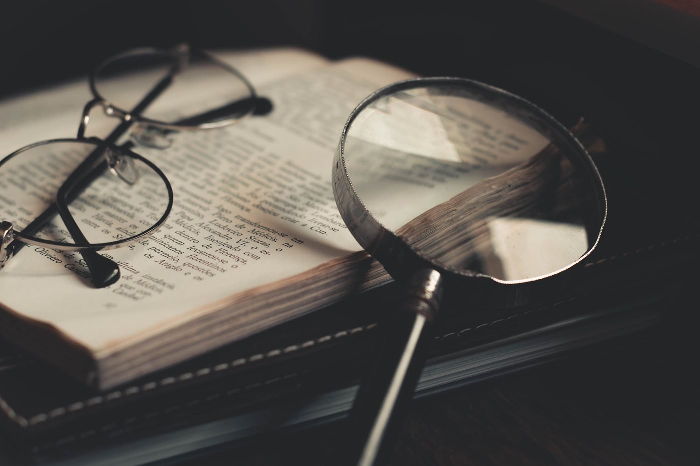 Open book with reading glasses and a magnifying glass, representing close research and insight